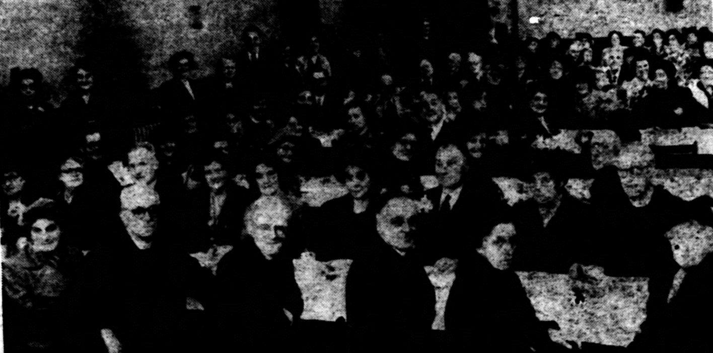 A group of people sitting in front of a sign
Description automatically generated